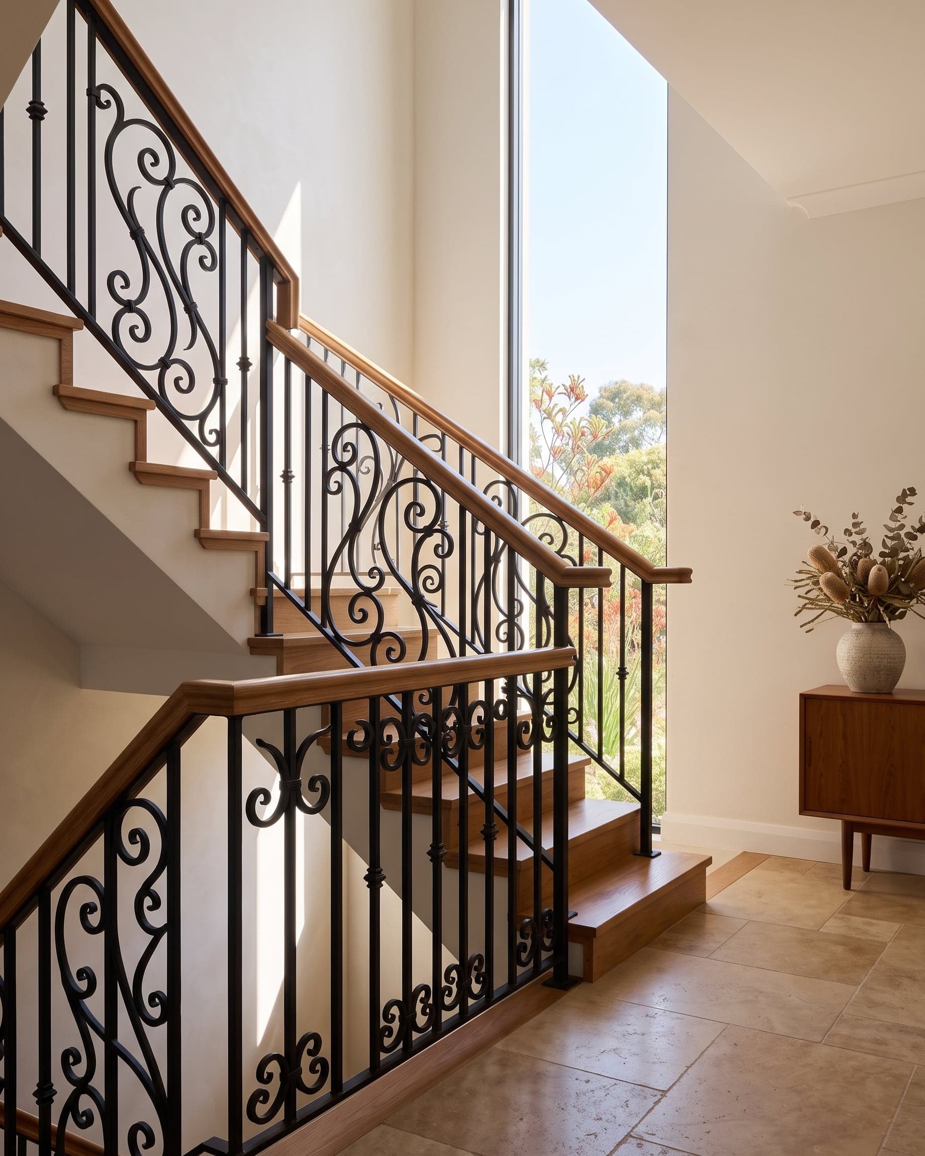 Interior staircase with a hand-forged matte-black wrought-iron balustrade, lit by a tall window onto a native garden